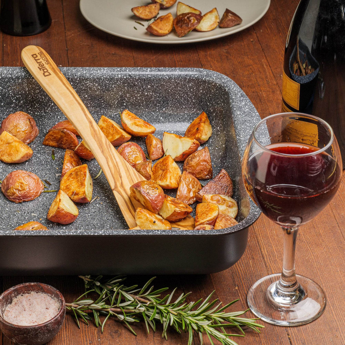 Roasted potatoes in a DaTerra Cucina ceramic pan, served with a glass of red wine and rosemary